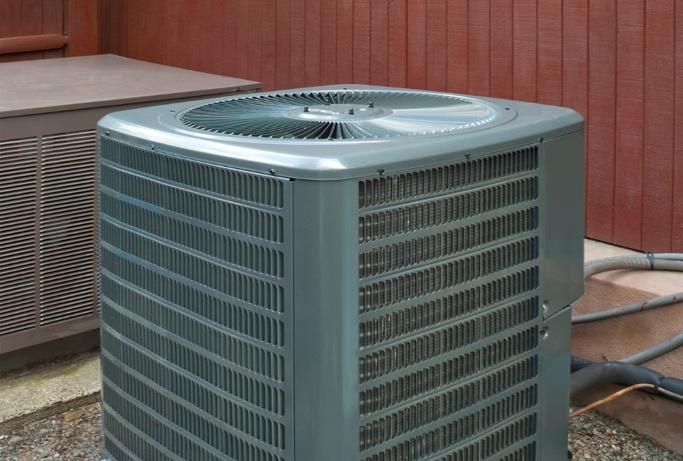 Close-up of a residential air conditioner unit in front of a red fence, showing signs of reduced cooling performance—ideal for topics like "air conditioner not blowing cold air," AC repair services, refrigerant issues, and HVAC maintenance by Arctic Air. Call today for help with air conditioner not blowing cold air, AC not cooling, air conditioner blowing warm air, AC blowing hot air instead of cold, home AC not working, HVAC repair near me, AC repair near me, air conditioning service near me, central air not cooling, fix my AC, Freon recharge near me, low refrigerant symptoms, AC compressor issues, broken AC capacitor, residential HVAC repair, emergency AC repair, AC maintenance near me, air conditioning troubleshooting, HVAC company near me, Arctic Air HVAC services, thermostat not working, AC unit not turning on, cooling system repair, heating and air conditioning service, HVAC technician near me.