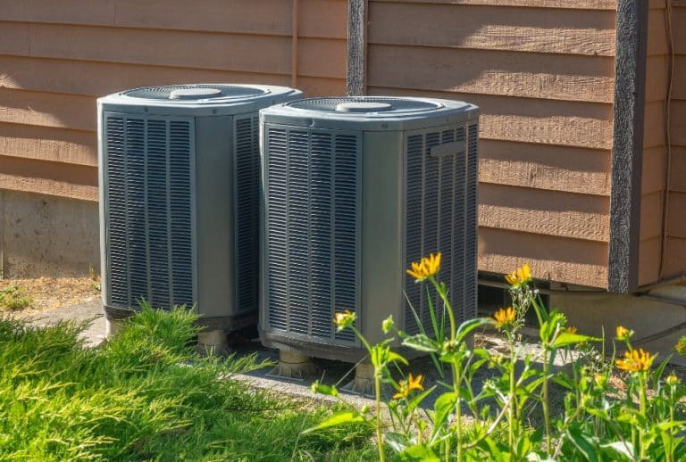 Outdoor residential AC unit surrounded by yellow flowers, representing common HVAC issues like a bad AC capacitor, air conditioner not starting, and home cooling problems; related to Arctic Air’s AC repair and capacitor replacement services. Trust us to help with bad AC capacitor symptoms, can AC run with a bad capacitor, signs of bad HVAC capacitor, AC not blowing cold air capacitor, air conditioner humming but not starting, capacitor failure in air conditioner, replace AC capacitor near me, HVAC capacitor repair near me, air conditioner not working capacitor issue, residential AC capacitor problems, home AC repair near me, AC won't turn on bad capacitor, emergency HVAC repair, AC capacitor replacement cost, HVAC technician near me, local AC repair services, Arctic Air air conditioning repair, HVAC maintenance services, heating and cooling repair near me, AC electrical problems, air conditioning not cooling properly, run capacitor vs start capacitor failure, AC making clicking sound won't start.
