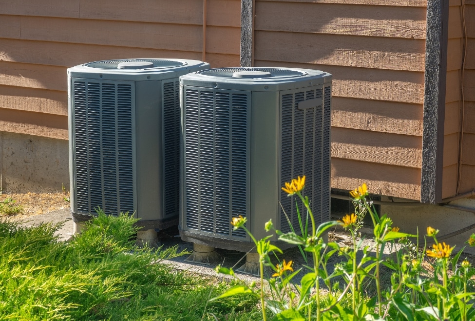 Outdoor residential AC unit surrounded by yellow flowers, representing common HVAC issues like a bad AC capacitor, air conditioner not starting, and home cooling problems; related to Arctic Air’s AC repair and capacitor replacement services. Trust us to help with bad AC capacitor symptoms, can AC run with a bad capacitor, signs of bad HVAC capacitor, AC not blowing cold air capacitor, air conditioner humming but not starting, capacitor failure in air conditioner, replace AC capacitor near me, HVAC capacitor repair near me, air conditioner not working capacitor issue, residential AC capacitor problems, home AC repair near me, AC won't turn on bad capacitor, emergency HVAC repair, AC capacitor replacement cost, HVAC technician near me, local AC repair services, Arctic Air air conditioning repair, HVAC maintenance services, heating and cooling repair near me, AC electrical problems, air conditioning not cooling properly, run capacitor vs start capacitor failure, AC making clicking sound won't start.
